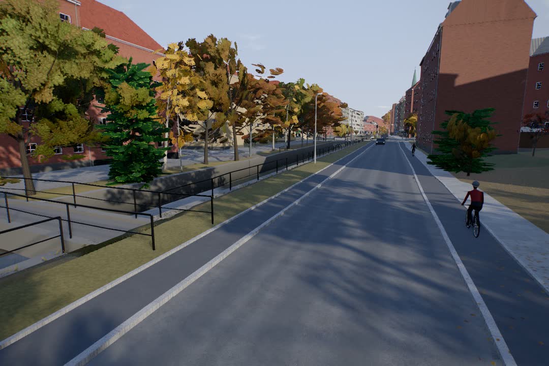 En bygade med cykelstier og træer i efterårsfarver mellem røde murstensbyggerier, med en cyklist på stien.